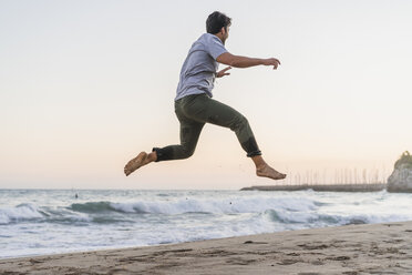 Happy young man jumping in the air on the beach at sunset - AFVF00160