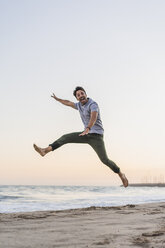 Happy young man jumping in the air on the beach at sunset - AFVF00161