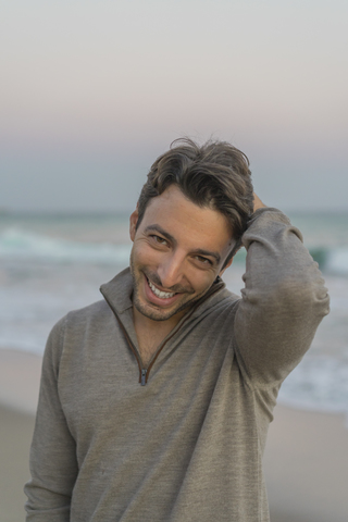 Porträt eines lächelnden jungen Mannes am Strand in der Dämmerung, lizenzfreies Stockfoto