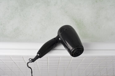 Ein Haartrockner, der auf dem Rand einer vollen Badewanne balanciert - FSIF02641