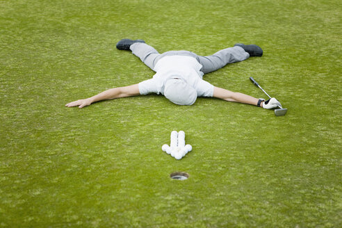 Ein Golfer, der auf einem Putting Green hinter einem Pfeil aus Golfbällen liegt - FSIF02643