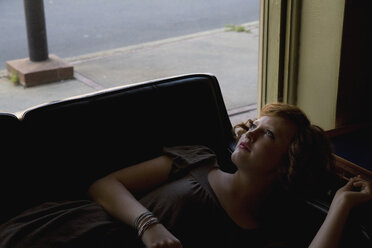 A young woman lying down on a sofa next to a window - FSIF02644