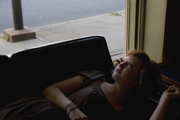 Eine junge Frau, die auf einem Sofa neben einem Fenster liegt - FSIF02644