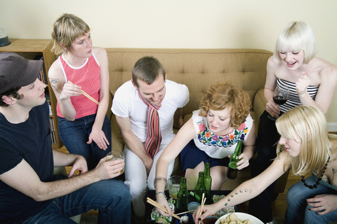Eine Gruppe von Freunden beim Essen und Trinken in einem Wohnzimmer, lizenzfreies Stockfoto