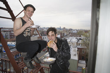 Two young men eating take out food on a fire escape - FSIF02654