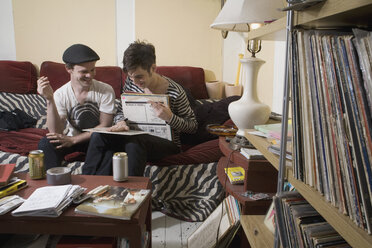 Zwei junge Männer schauen sich auf einem Sofa Platten an - FSIF02655