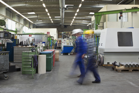 Zwei Arbeiter gehen durch eine Fabrik, unscharfe Bewegung, Langzeitbelichtung, lizenzfreies Stockfoto