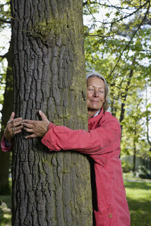 Eine ältere Frau umarmt einen Baum - FSIF02672