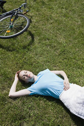 A young woman lying in grass near a bicycle - FSIF02693