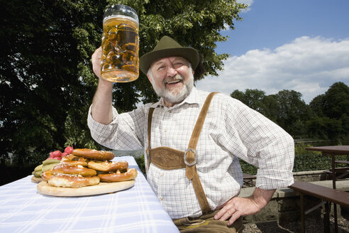 A traditionally clothed German man in a beer garden raising his beer glass in toast - FSIF02696