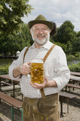 Ein traditionell gekleideter deutscher Mann in einem Biergarten, der ein Bierglas hält - FSIF02697