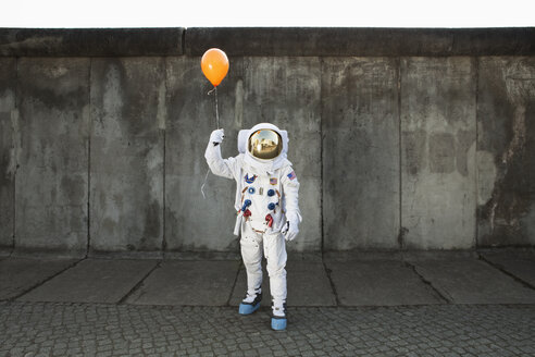 An astronaut on a city sidewalk holding a balloon - FSIF02768