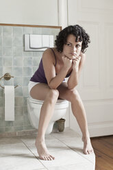 Eine Frau, die auf der Toilette sitzt und unglücklich aussieht - FSIF02795