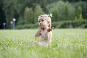 Ein kleines Mädchen sitzt in einer Windel im Gras und schaut verwirrt - FSIF02804