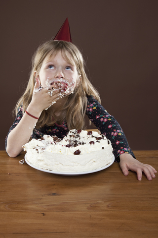 Ein Mädchen mit einem Partyhut isst Kuchen mit den Händen, Studioaufnahme, lizenzfreies Stockfoto