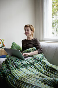 Eine Frau, die sich auf einer Couch zurücklehnt und einen Laptop benutzt - FSIF02841