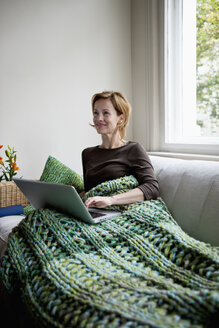 A woman reclining on a couch using a laptop - FSIF02841