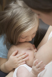 Eine Mutter, die ihr Kind stillt, während ihre Tochter den Kopf des Kindes hält - FSIF02860