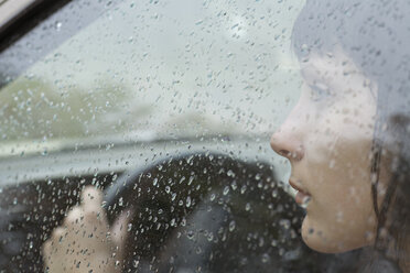 Eine Autofahrerin sitzt im Auto und schaut aus dem Fenster, Regentropfen auf dem Fenster - FSIF02876
