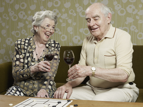 Ein älteres Paar trinkt Rotwein und stößt auf der Couch an, lizenzfreies Stockfoto