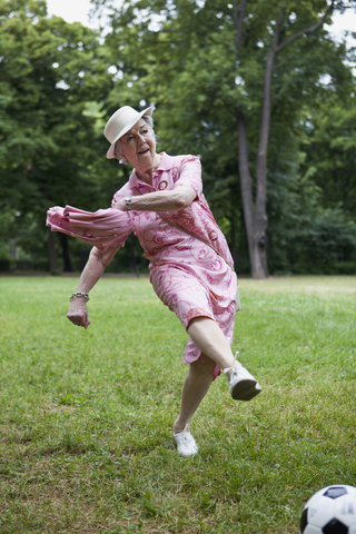 Seniorin kickt Fußball im Park, lizenzfreies Stockfoto