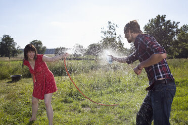 Mann und Frau bespritzen sich auf einem Feld gegenseitig mit Wasser - FSIF02896