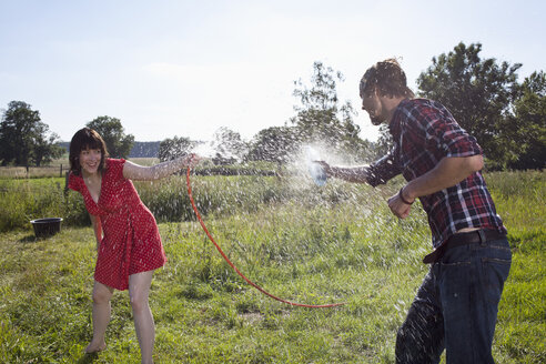 Mann und Frau bespritzen sich auf einem Feld gegenseitig mit Wasser - FSIF02896