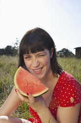 Girl sitting in field with a slice of melon in her hand - FSIF02903