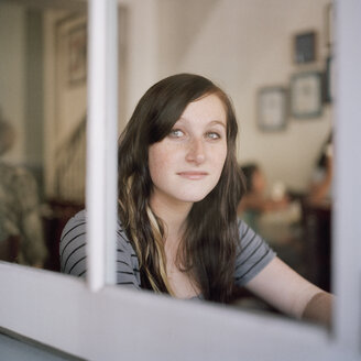 Eine junge Frau schaut nachdenklich durch ein Fenster - FSIF02938