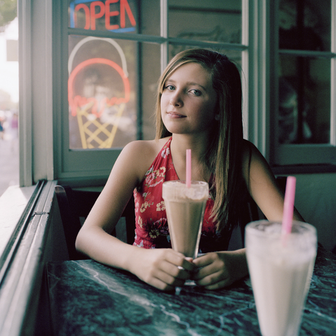 Ein junges Mädchen sitzt mit einem Milchshake am Tisch, lizenzfreies Stockfoto