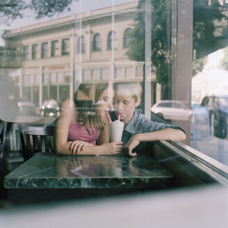 A young teenage couple sharing a milkshake at a diner, viewed through window - FSIF02950