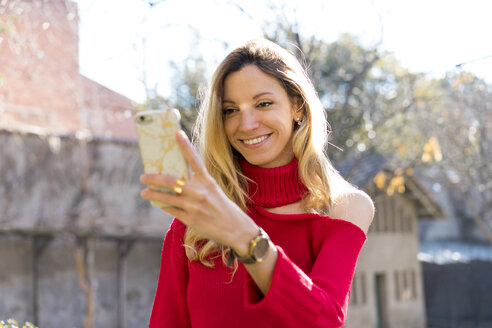 Porträt einer lächelnden jungen Frau mit Blick auf ihr Smartphone im Freien - AFVF00180