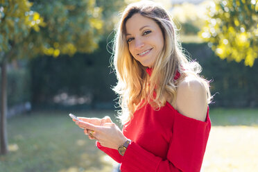 Portrait of smiling young woman using smartphone in a garden - AFVF00189
