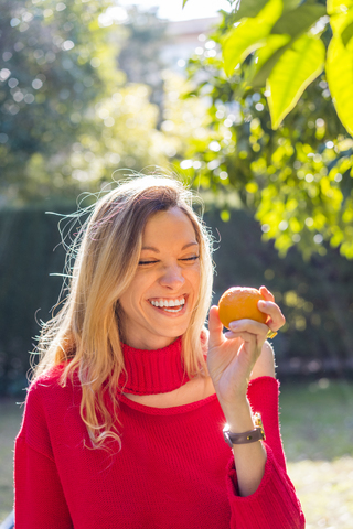 Lachende junge Frau mit Mandarine in einem Garten, lizenzfreies Stockfoto