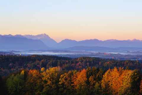 Deutschland, Bayern, Oberbayern, Alpenvorland, Kirchturm von Königsdorf, Zugspitze und Ammergauer Alpen bei Sonnenaufgang, Blick von der Peretshofener Höhe im Herbst, lizenzfreies Stockfoto