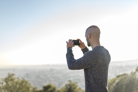 Young man standing on a hill taking cell phone picture stock photo