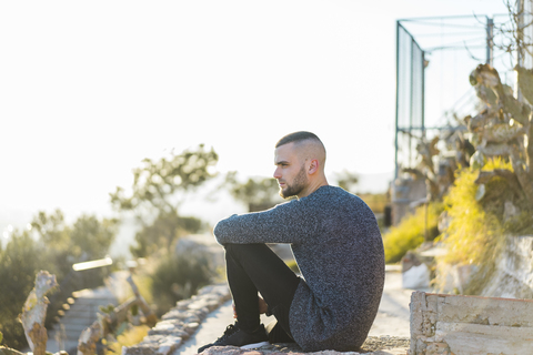 Ernster junger Mann sitzt auf einer Mauer, lizenzfreies Stockfoto