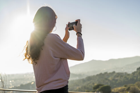 Junge Frau steht auf einem Hügel und macht ein Handyfoto - AFVF00211