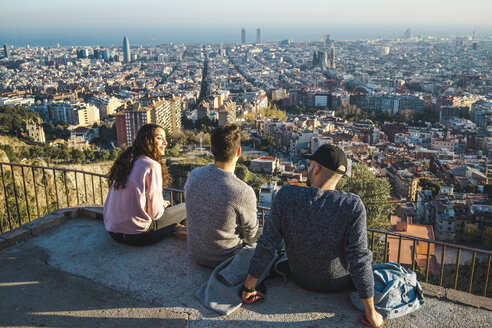 Spanien, Barcelona, drei Freunde sitzen auf einer Mauer mit Blick auf die Stadt - AFVF00217