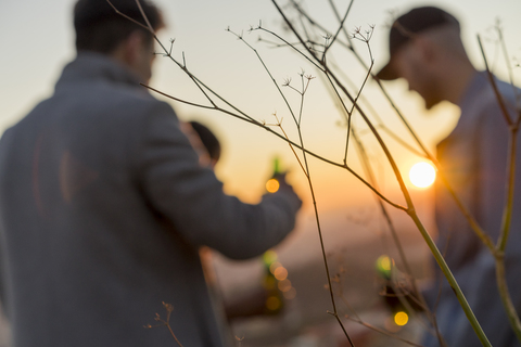 Defocused view of friends with beer bottles outdoors at sunset stock photo