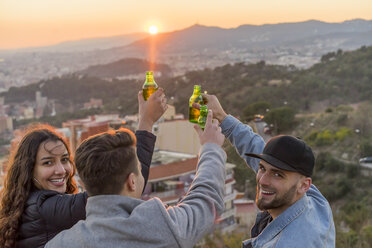 Spanien, Barcelona, drei glückliche Freunde mit Bierflaschen auf einem Hügel mit Blick auf die Stadt bei Sonnenuntergang - AFVF00222