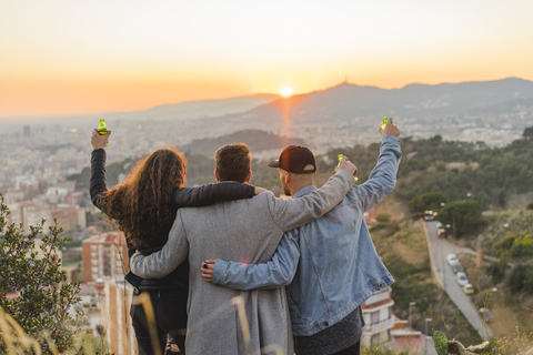 Spain, Barcelona, three friends with beer bottles embracing on a hill overlooking the city at sunset stock photo