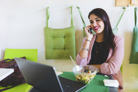 Junge Geschäftsfrau beim gesunden Mittagessen mit Handy und Laptop, lizenzfreies Stockfoto