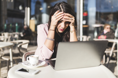 Frustrierte junge Geschäftsfrau mit Laptop in einem Straßencafé, lizenzfreies Stockfoto