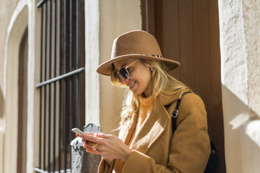 Modische junge Frau am Hauseingang mit Mobiltelefon - AFVF00229