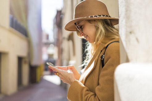 Modische junge Frau in einer Gasse mit Mobiltelefon - AFVF00232