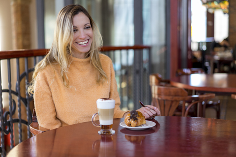 Glückliche junge Frau in einem Café, die Gebäck und Kaffee genießt, lizenzfreies Stockfoto