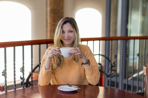 Porträt einer lächelnden jungen Frau in einem Café, die einen Kaffee genießt, lizenzfreies Stockfoto