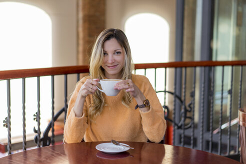 Porträt einer lächelnden jungen Frau in einem Café, die einen Kaffee genießt - AFVF00243