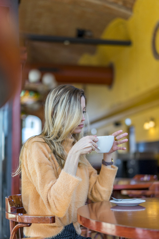 Nachdenkliche junge Frau in einem Cafe mit einer Tasse Kaffee in der Hand, lizenzfreies Stockfoto